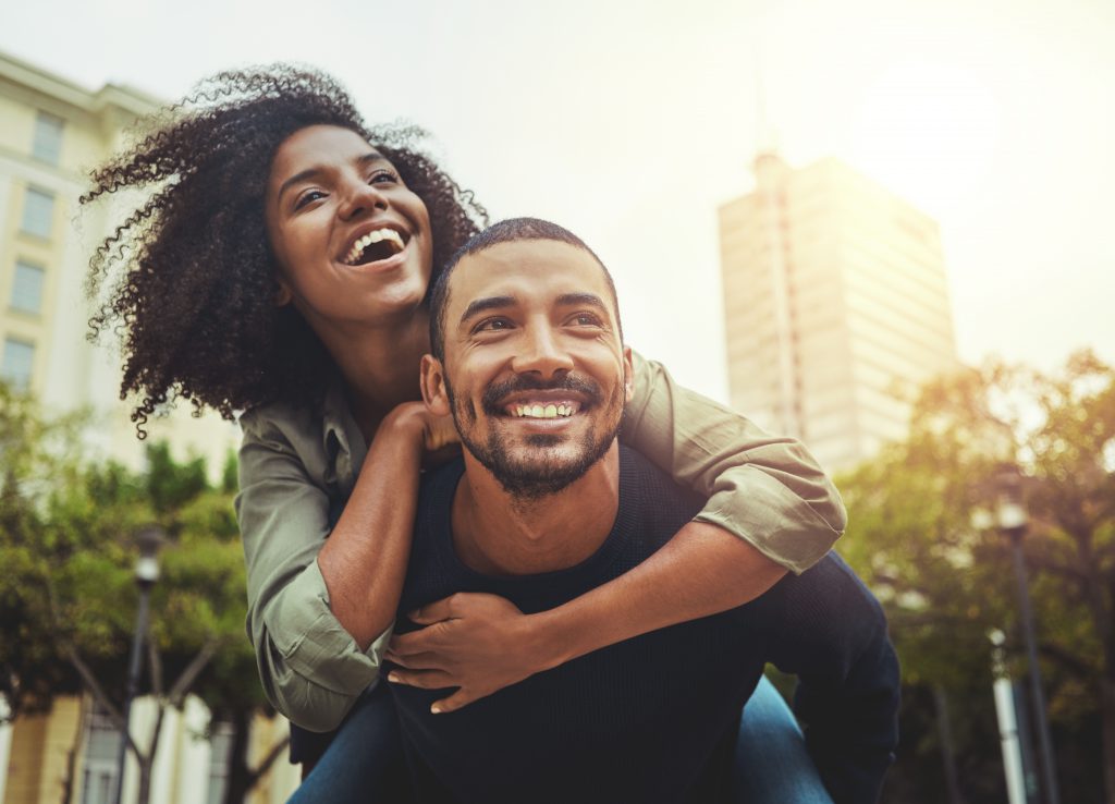 Cheerful young man giving piggyback ride to his girlfriend outdoors in the city